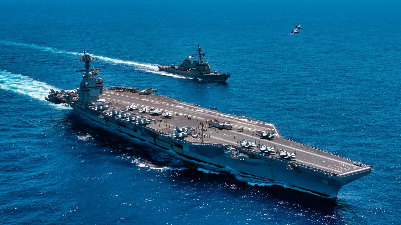 An F/A-18F Super Hornet, attached to the "Blacklions" of Strike Fighter Squadron (VFA) 213 and a F/A-18E Super Hornet, attached to the "Golden Warriors" of Strike Fighter Squadron (VFA) 87 fly over the world's largest aircraft carrier, USS Gerald R. Ford (CVN 78), the Arleigh Burke-class guided-missile destroyer USS Mahan (DDG 72), April 11, 2025. The Gerald R. Ford Carrier Strike Group is underway in the Atlantic Ocean completing integrated naval warfighting training. Composite Training Unit Exercise (COMPTUEX) is the Joint Force’s most complex integrated training event and prepares naval task forces for sustained high-end Joint and combined combat. Integrated naval training provides America’s civilian leaders and commanders highly-capable forces that deter adversaries, underpin American security and economic prosperity, and reassure Allies and partners. (U.S. Navy photo by Mass Communication Specialist 2nd Class Maxwell Orlosky
